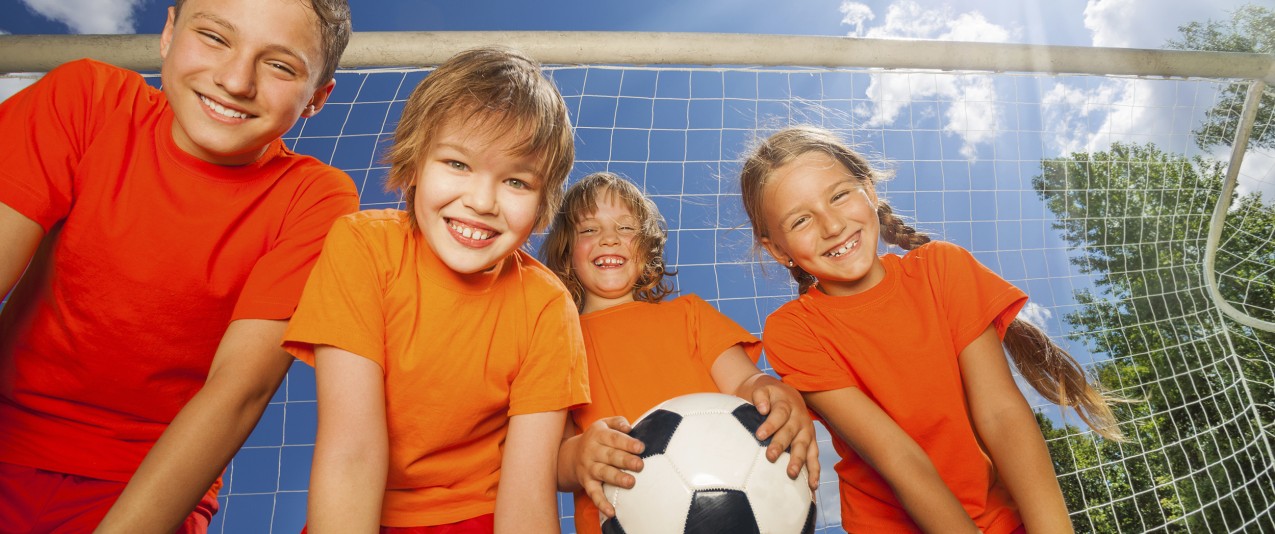 Four happy children with football portrait view from below in sunny weather